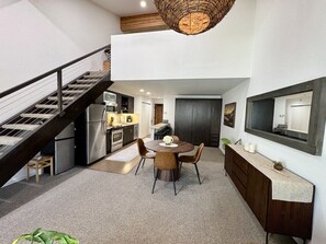 A modern kitchen with a dining area, a staircase, and a large mirror.