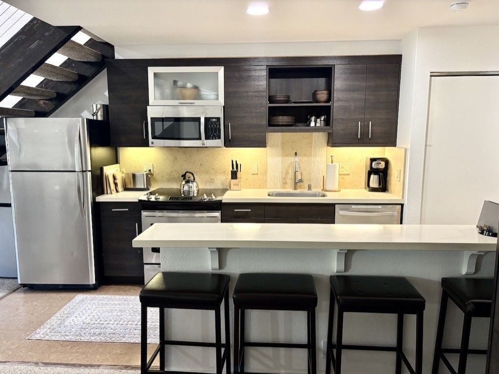 A modern kitchen with dark cabinetry, a stainless steel refrigerator, a microwave, and a coffee maker.