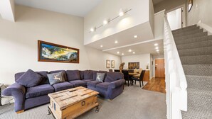 A modern living room with a sectional sofa, a wooden coffee table, and a staircase leading to an upper level. - 354 | Premium Loft Vibes - Oven, A/C + Pool (Olympic Valley)