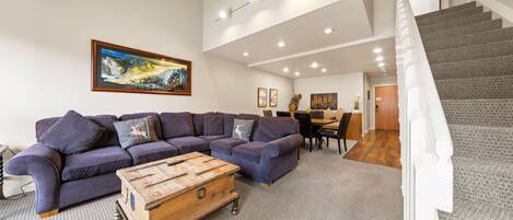 A modern living room with a sectional sofa, a wooden coffee table, and a staircase leading to an upper level.