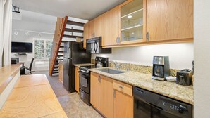 A compact kitchen with wooden cabinets, a stainless steel refrigerator, a microwave, a coffee maker, and a dishwasher.
