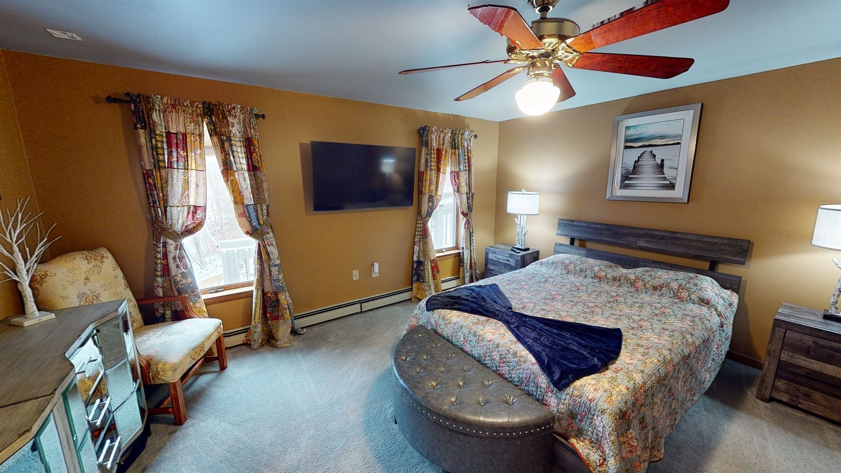 A hotel room with a bed, a desk, a chair, a ceiling fan, and a window with curtains.