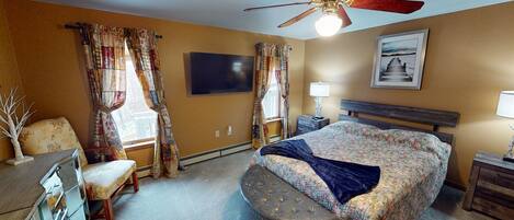 A hotel room with a bed, a desk, a chair, a ceiling fan, and a window with curtains.