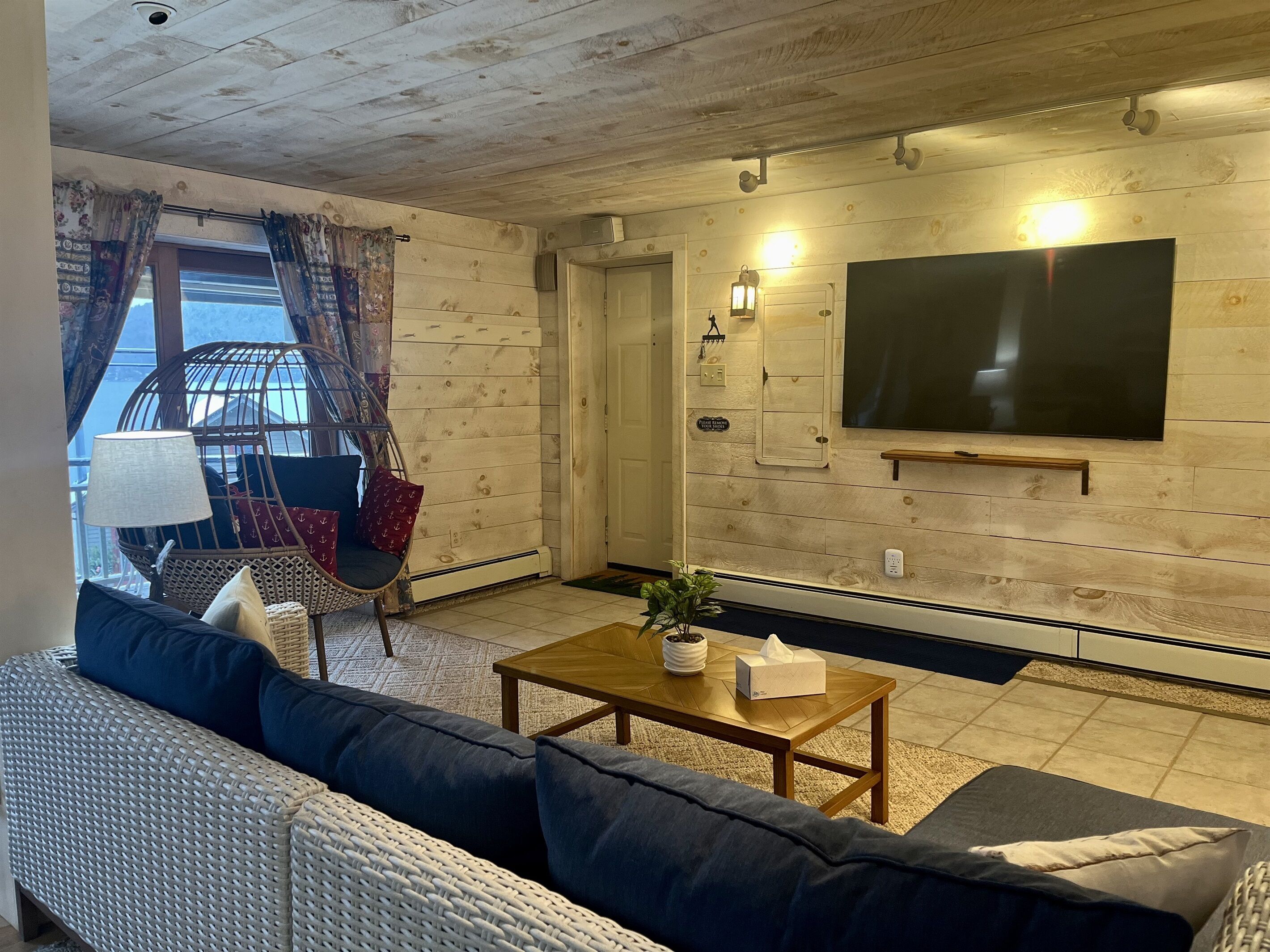 Un salon comprenant un canapé, un fauteuil, une table basse et un téléviseur fixé au mur.
