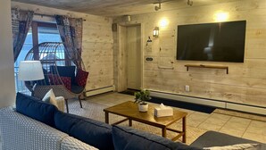 A living room with a sofa, a chair, a coffee table, and a TV mounted on the wall. - Lion View ~ Otsego Lake ~ Sleeps up to 10 (Cooperstown)