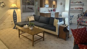 A cozy living room with a sofa, coffee table, and a dining area with a chair and table. - Lion View ~ Otsego Lake ~ Sleeps up to 10 (Cooperstown)