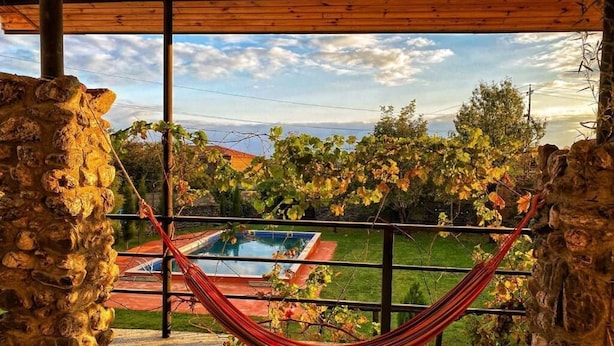 A hammock in a covered outdoor area with a view of a swimming pool and a garden. - Varga Kvareli (Kvareli)