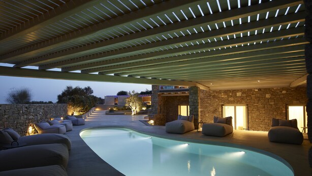 Un área de piscina moderna al aire libre con asientos integrados y un muro de piedra.