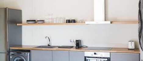 A compact kitchen with a washing machine, dishwasher, oven, and a countertop with a coffee maker and a kettle.