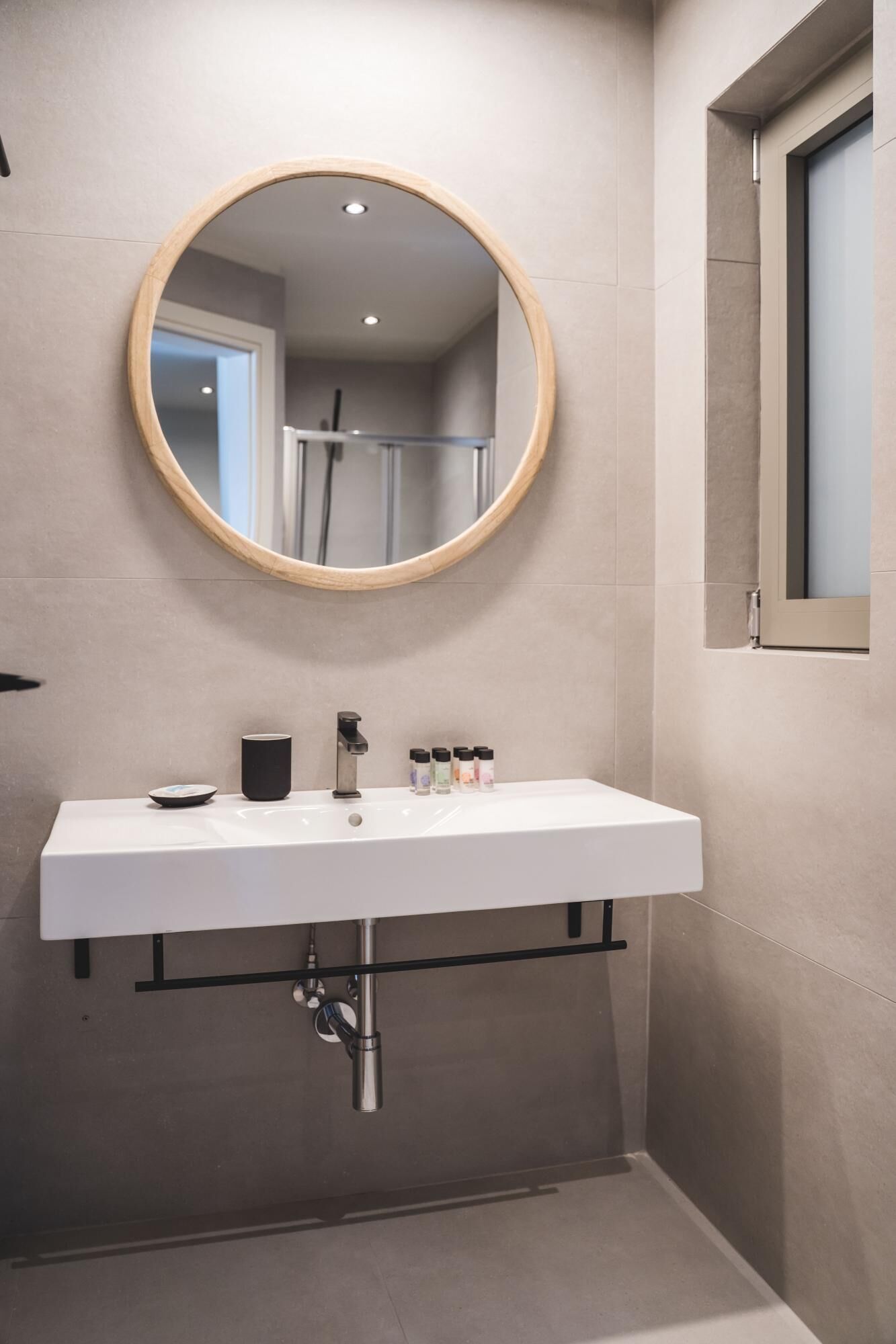 A modern bathroom with a round mirror, white sink, and a window.
