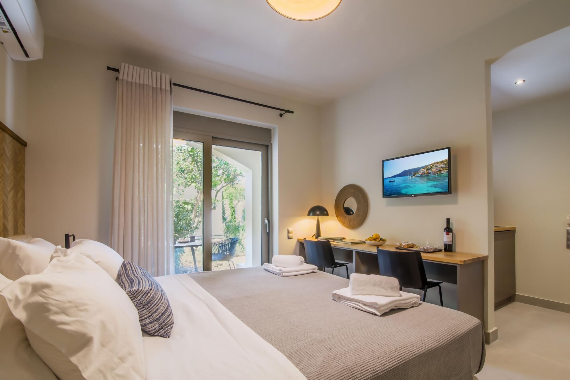 A modern hotel room with a large bed, a desk, and a TV displaying a scenic view.