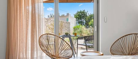 A room with a bed, two wicker chairs, a small table, and a view of the outside.