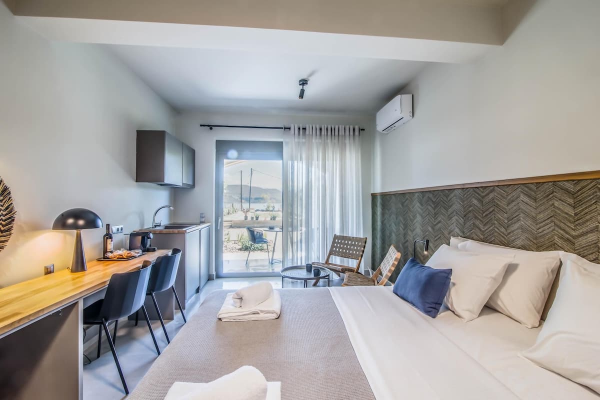 A hotel room with a bed, desk, chairs, and a view of the outdoors.