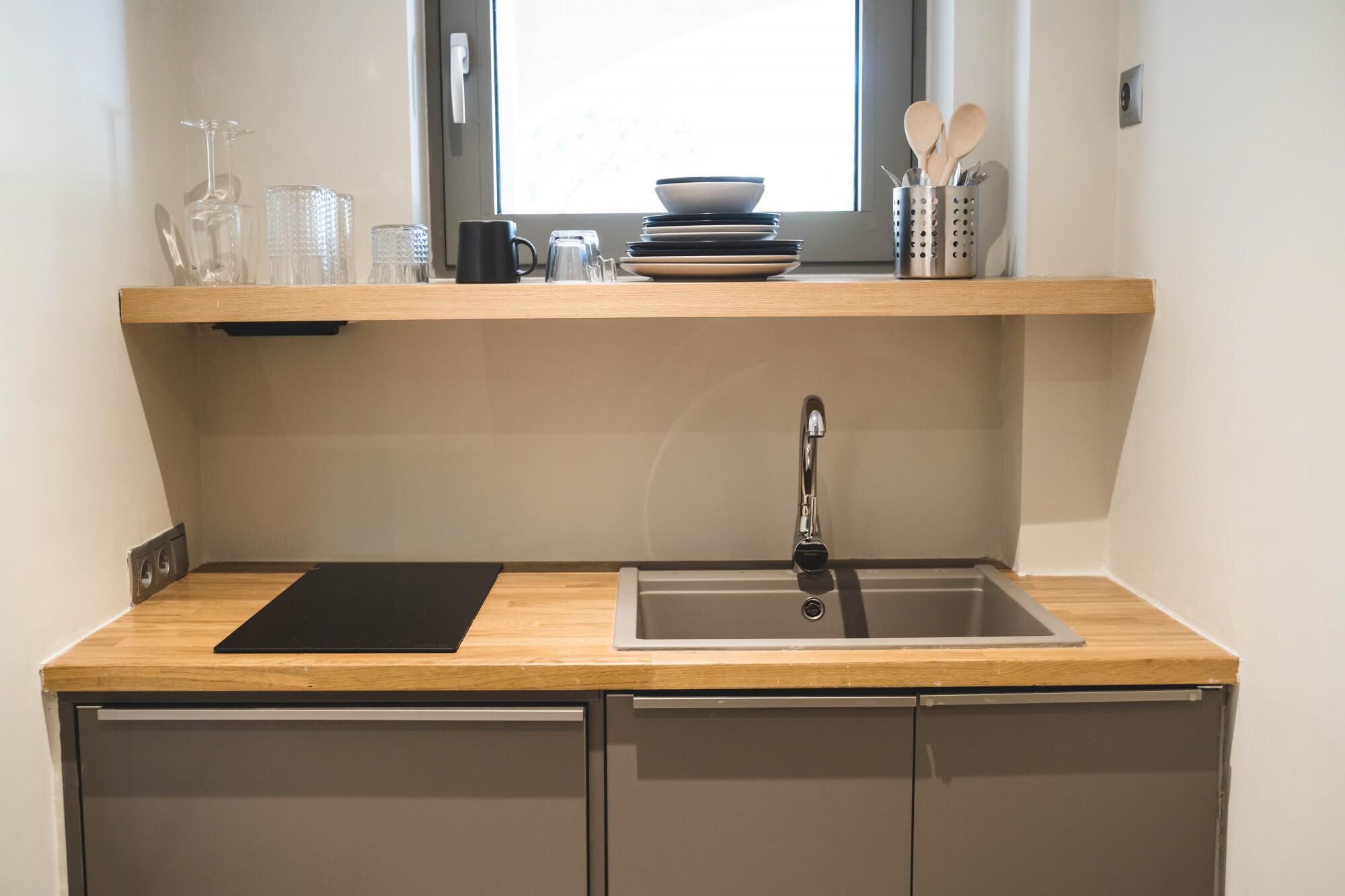 Een kleine keuken met een ingebouwd spoelgedeelte, een zwart snijplank en een raam boven het aanrecht.