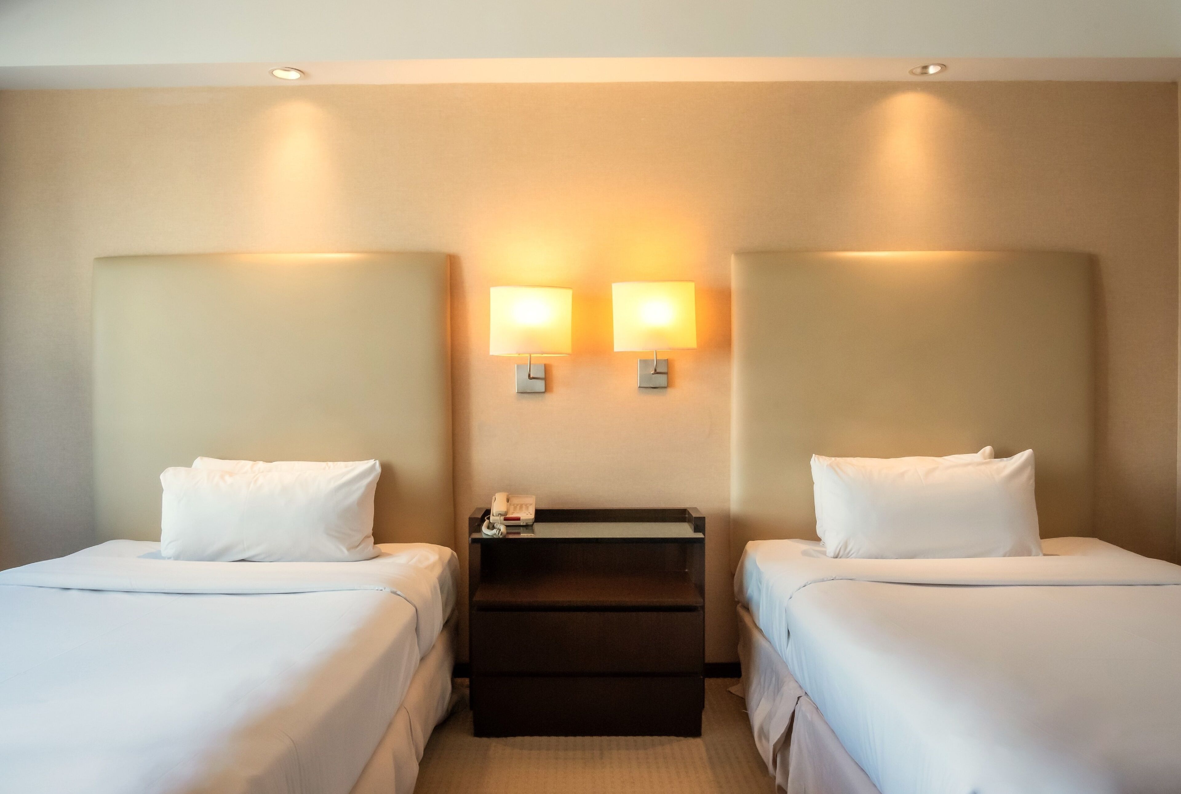 A hotel room with two single beds, a nightstand with a phone, and two wall-mounted lamps.