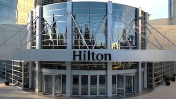 A modern Hilton hotel entrance with a glass facade, a revolving door, and a clear view of the surrounding buildings.