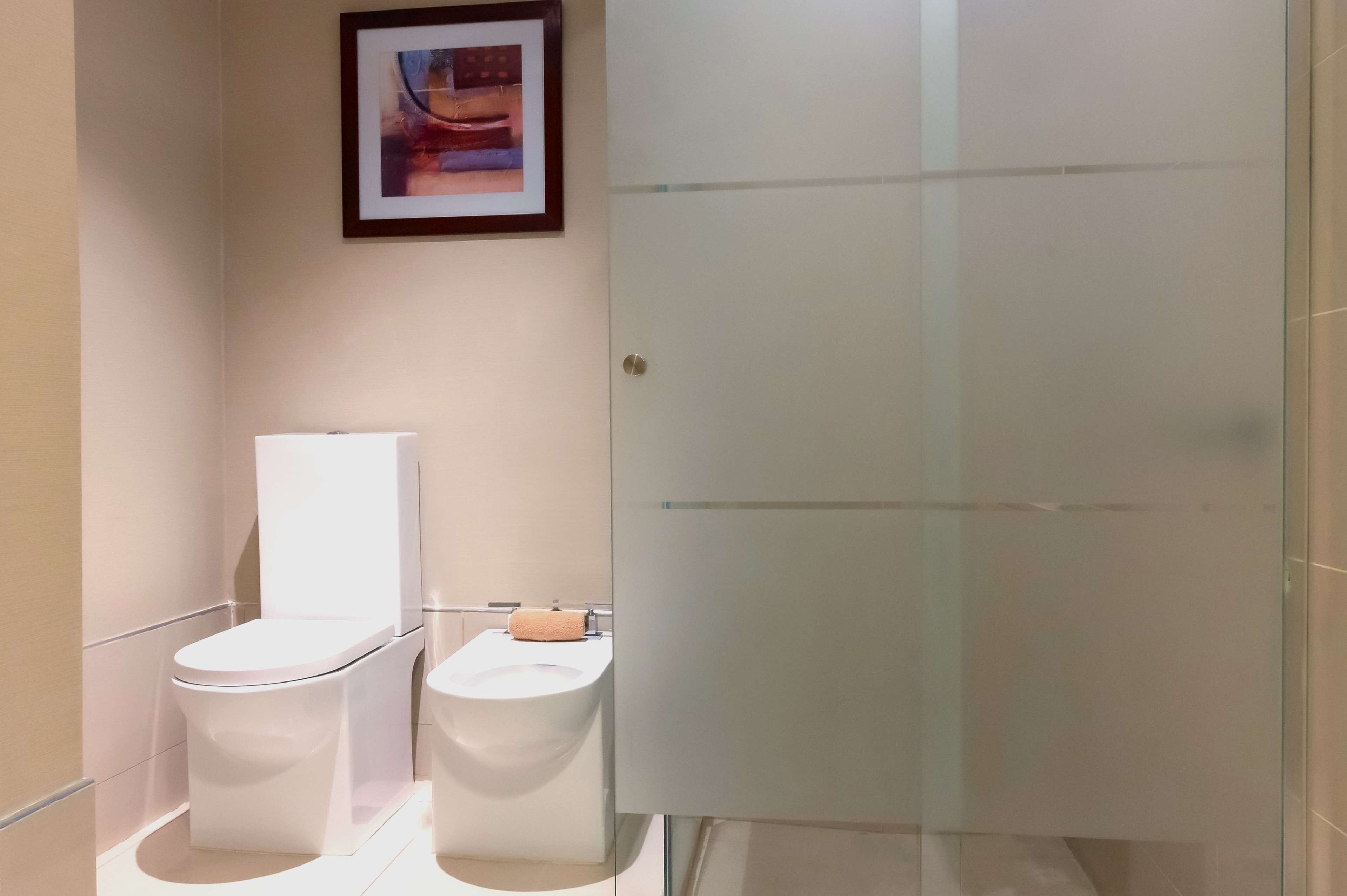Une salle de bain moderne avec deux toilettes, une douche en verre et un tableau encadré au mur.