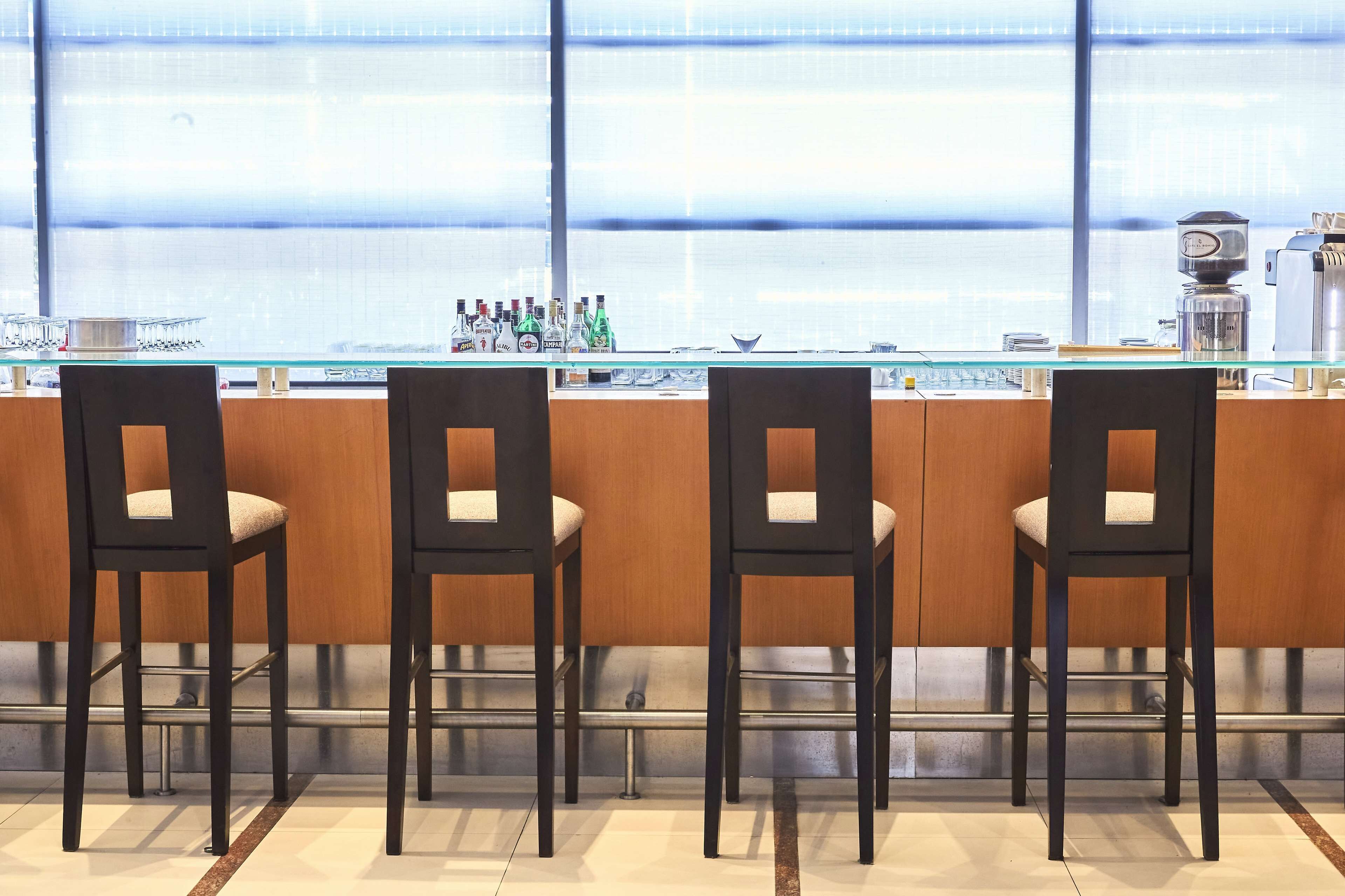 Una zona de bar con cuatro sillas de madera y un mostrador de cristal que exhibe varias botellas y copas.