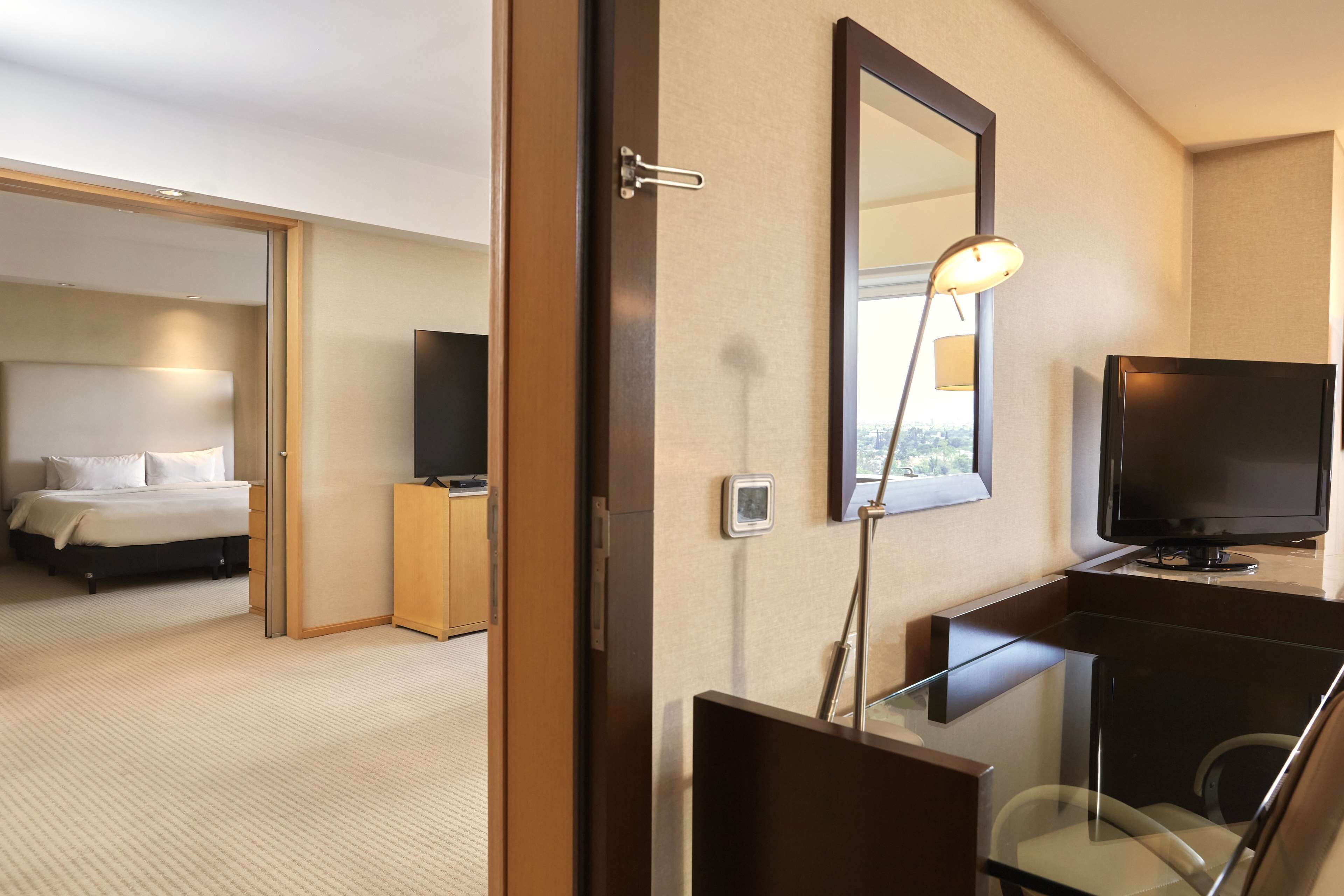 A hotel room with a bed, a desk with a computer, a TV, and a large mirror.
