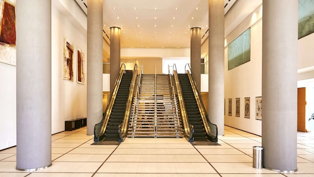 A spacious lobby with two escalators, large columns, and a tiled floor. - Hilton Mendoza (Guaymallen)