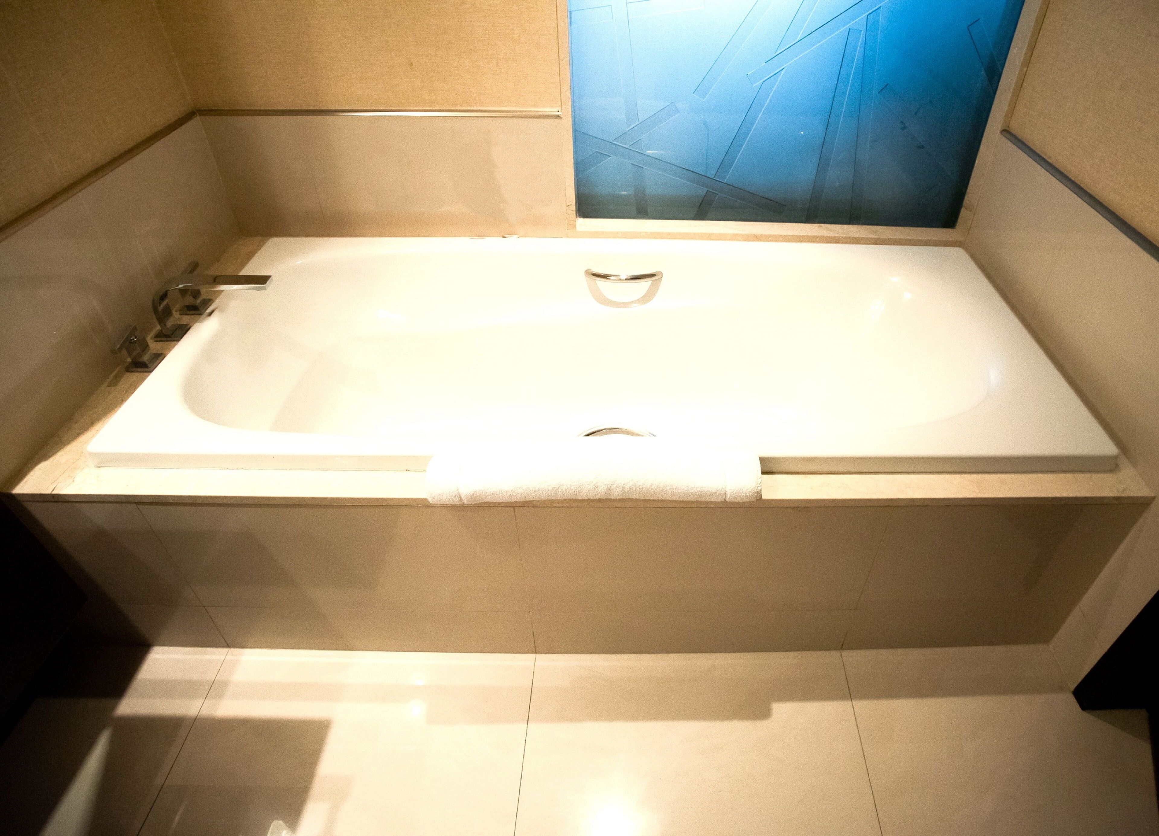 Una bañera grande y rectangular con un solo grifo y desagüe central, ubicada en un cuarto con paredes y piso de baldosas.