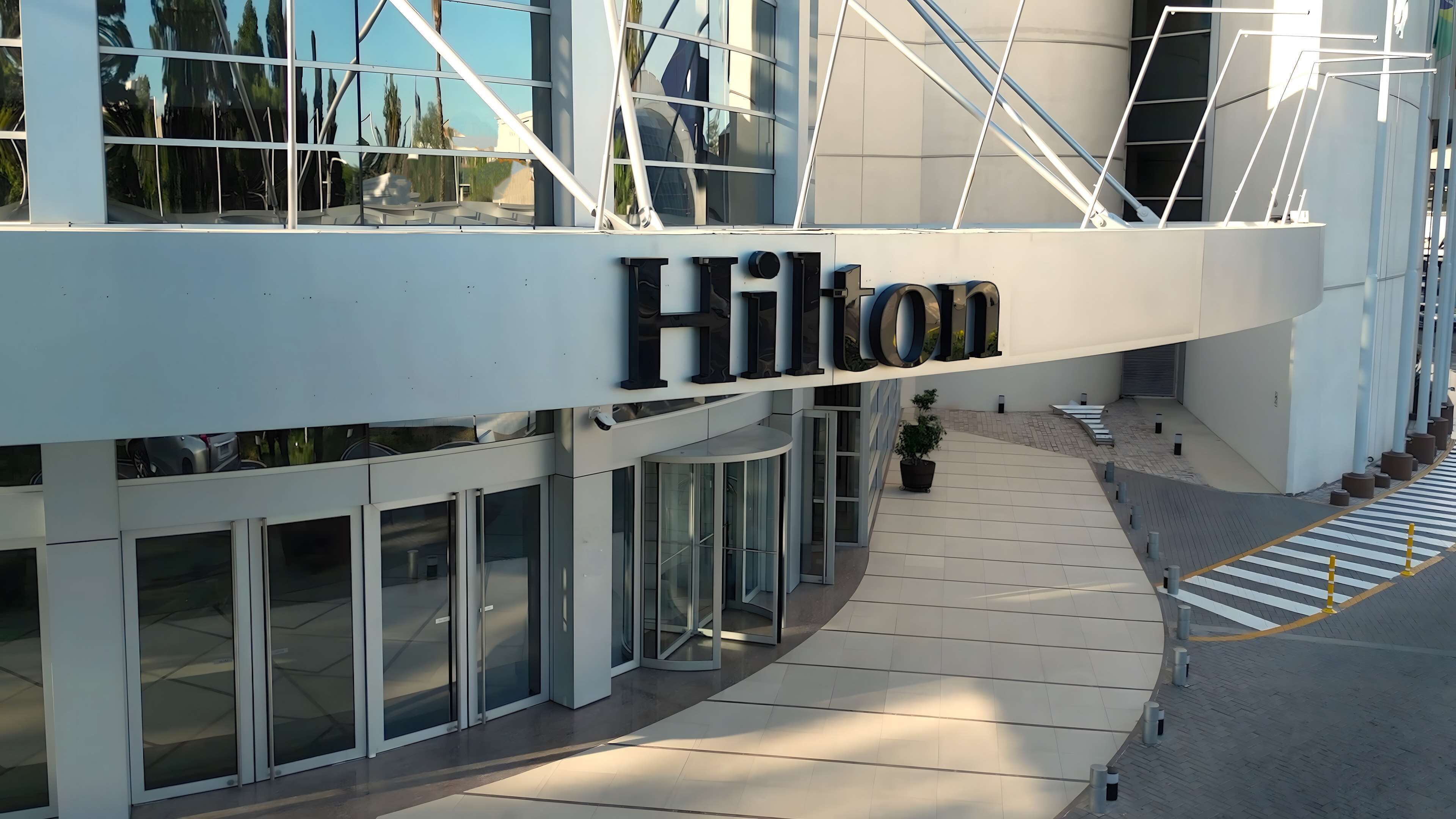 Exterior de un hotel Hilton con un diseño arquitectónico moderno, que cuenta con amplios ventanales y una señalización destacada.