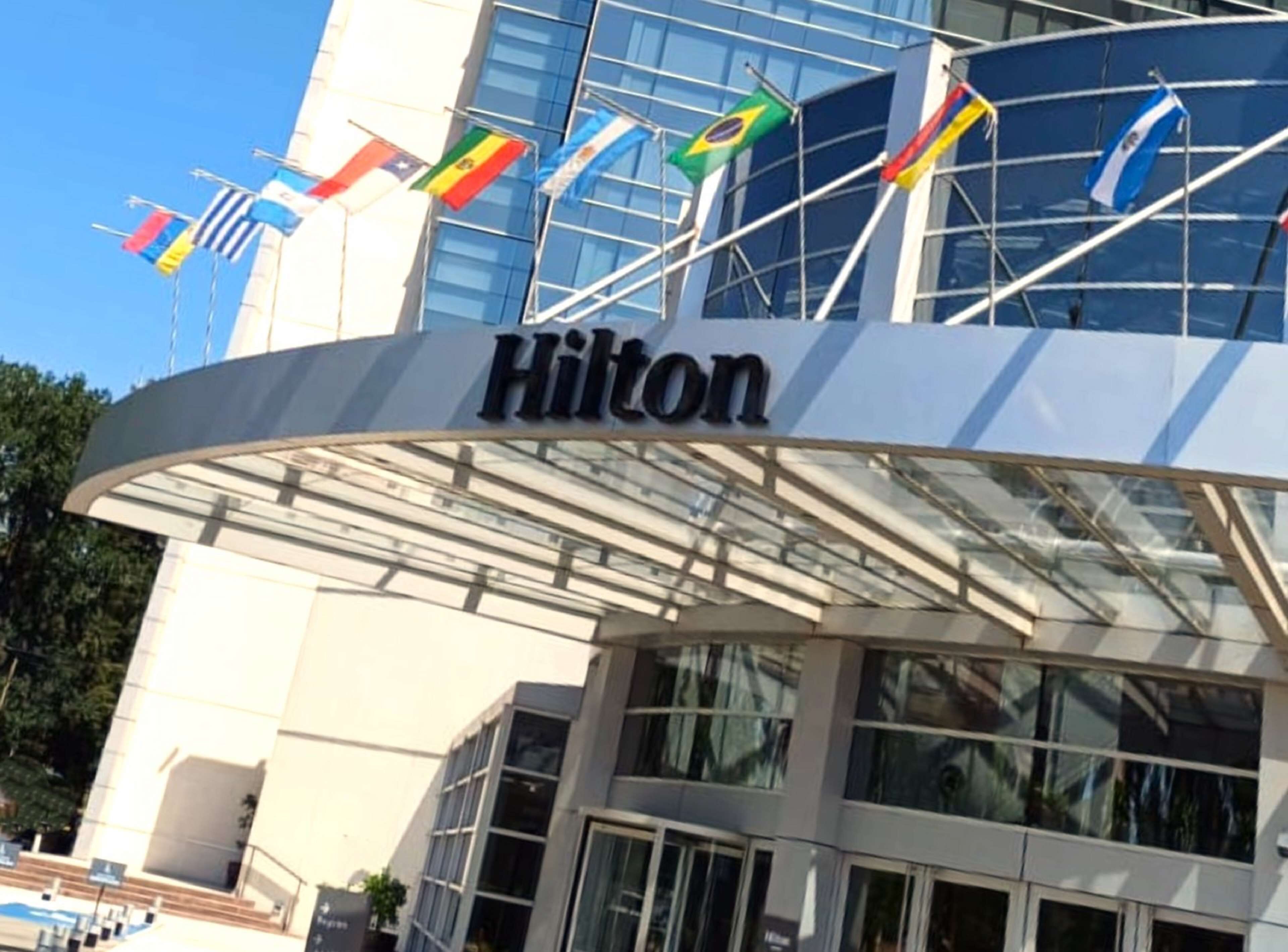 Edificio de un hotel Hilton con fachada de vidrio moderna y varias banderas en el exterior.