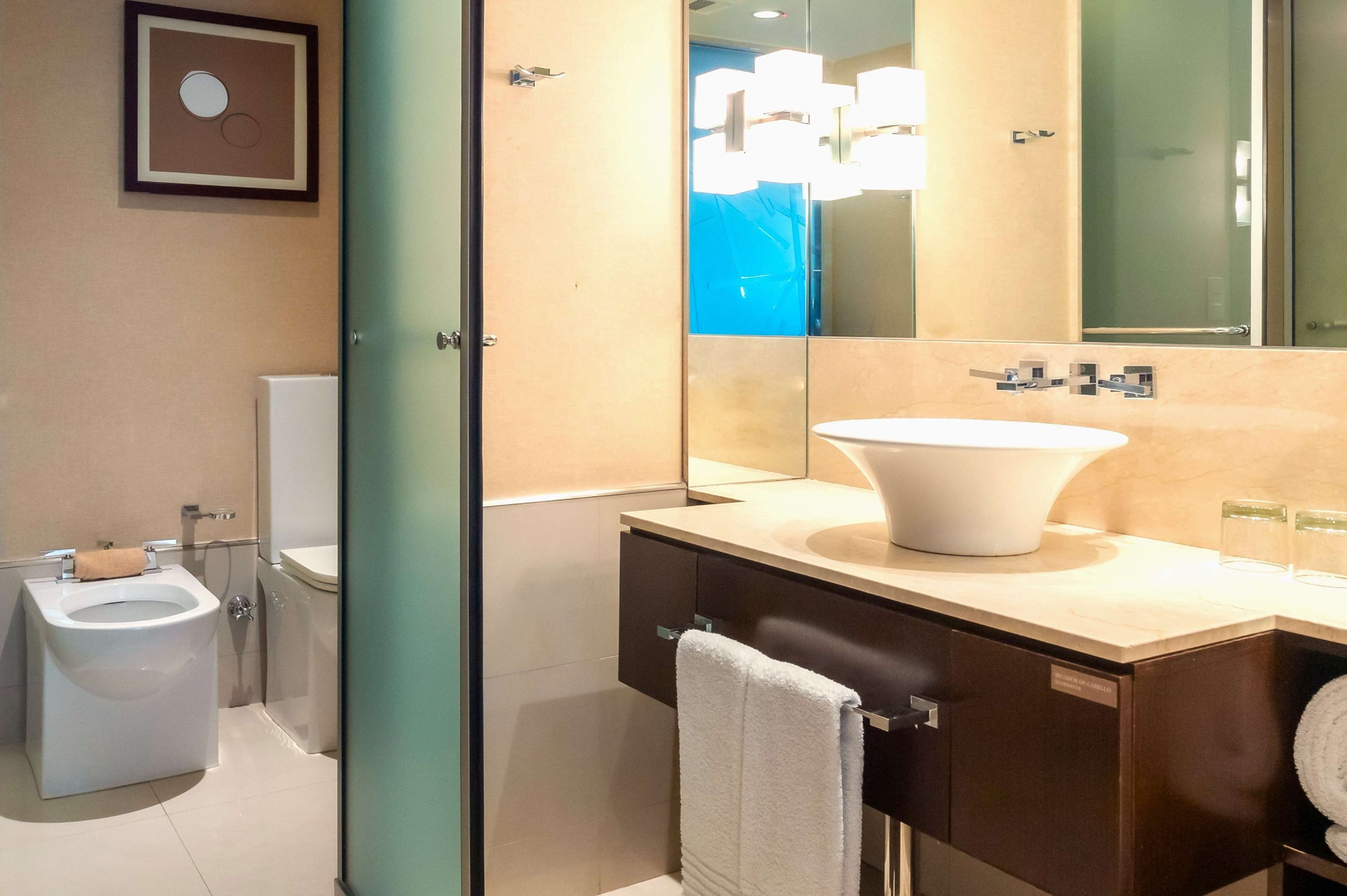 A modern bathroom with a toilet, bidet, sink, and mirror.