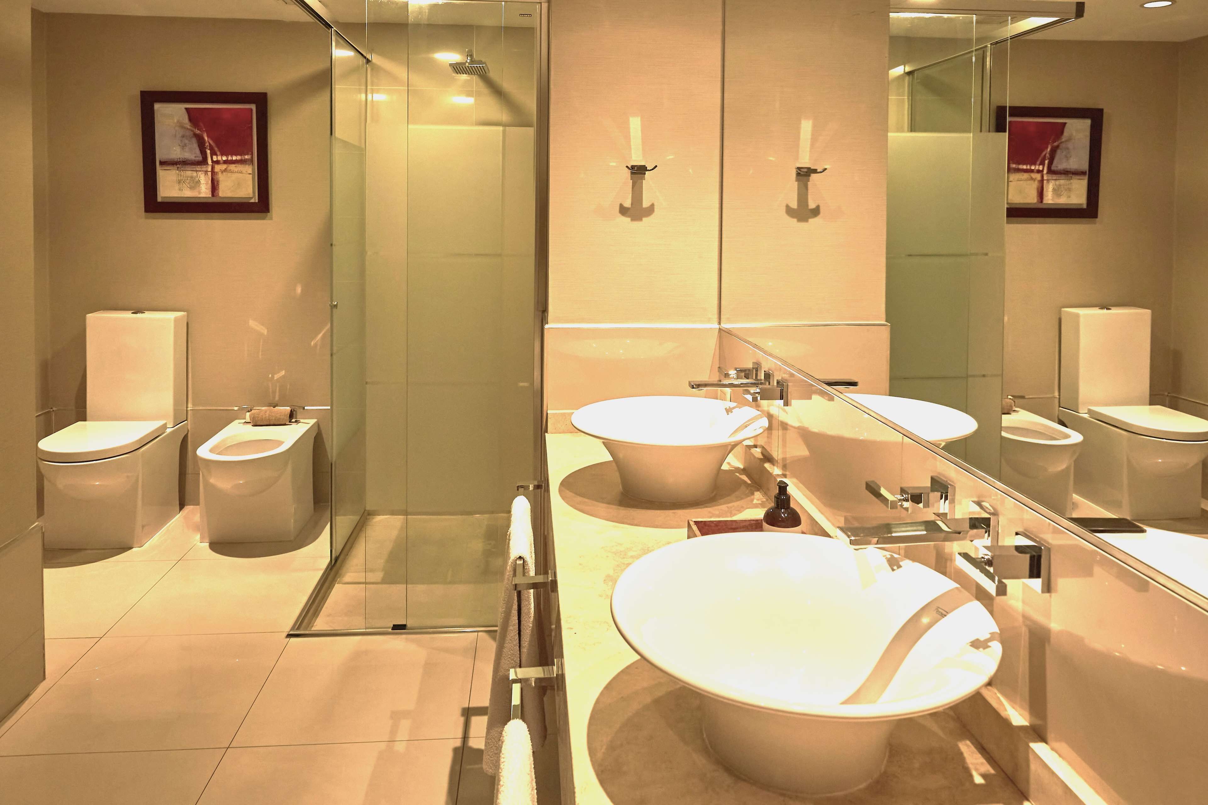 A modern bathroom with two toilets, a large sink, a glass shower enclosure, and a mirror reflecting the room.