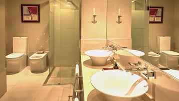 A modern bathroom with two toilets, a large sink, a glass shower enclosure, and a mirror reflecting the room.
