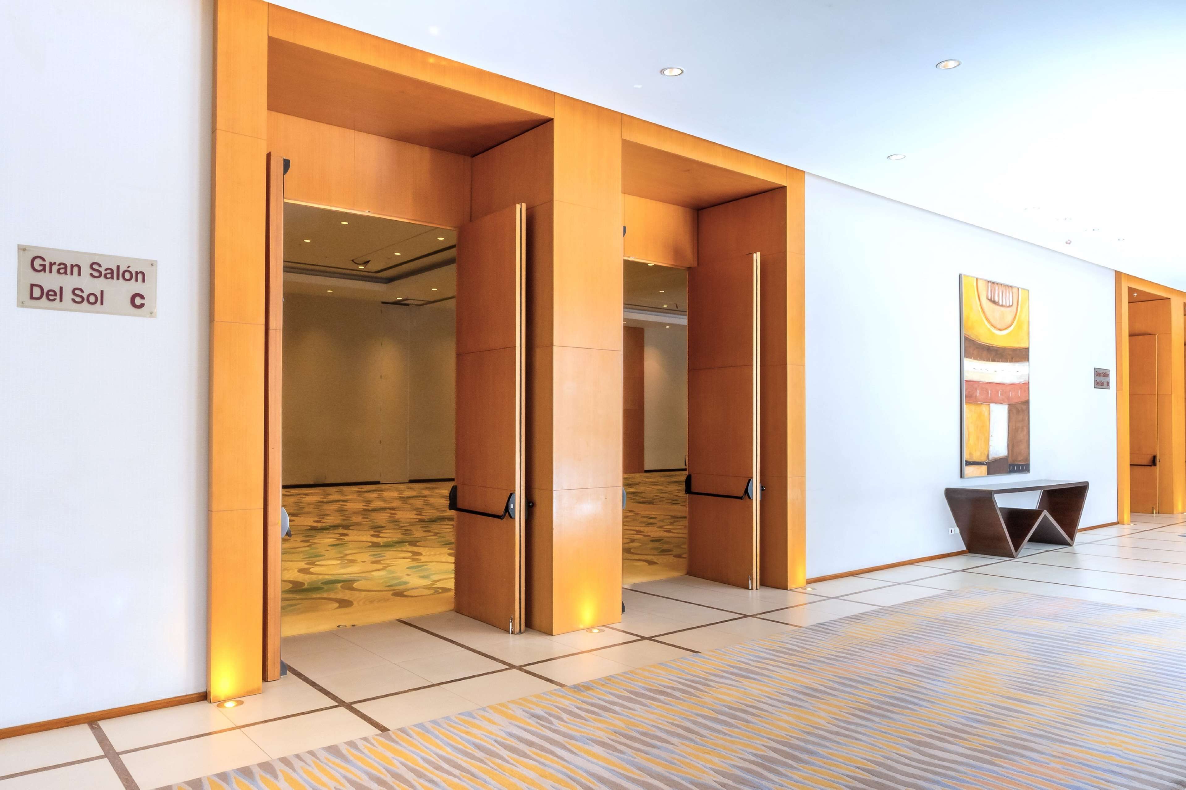 Un hall d’hôtel avec une enseigne indiquant « Gran Salón Del Sol », et un design moderne agrémenté d’éléments en bois et d’un sol à motifs.