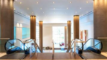 An interior view of a modern building with two escalators, large pillars, and a spacious area with a view to the outside.