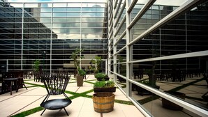 A modern building with a glass facade, outdoor seating area with chairs and planters, and a tiled floor. - Hilton Mendoza (Guaymallen)
