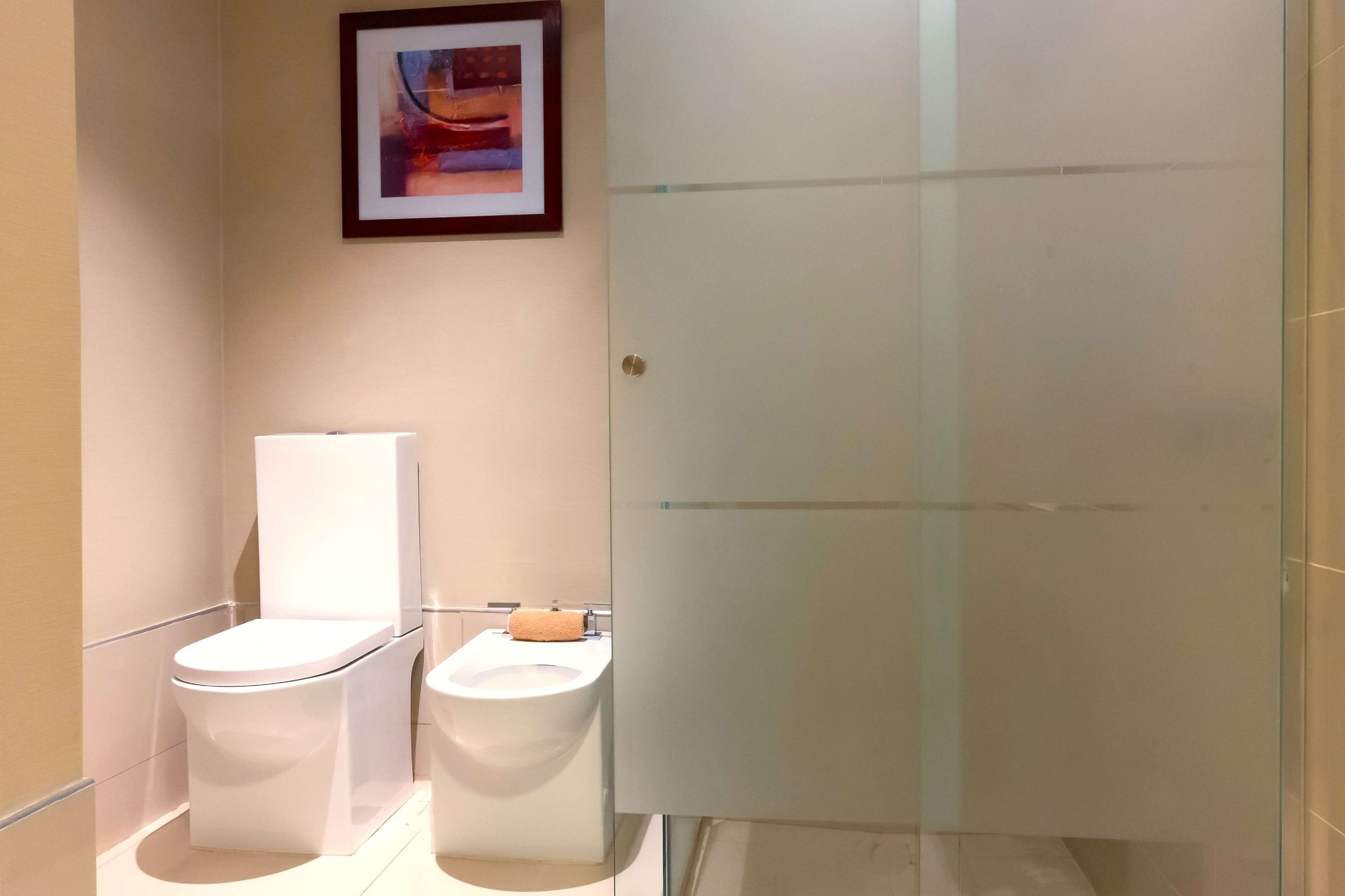 A modern bathroom with a toilet, bidet, and a glass shower enclosure.