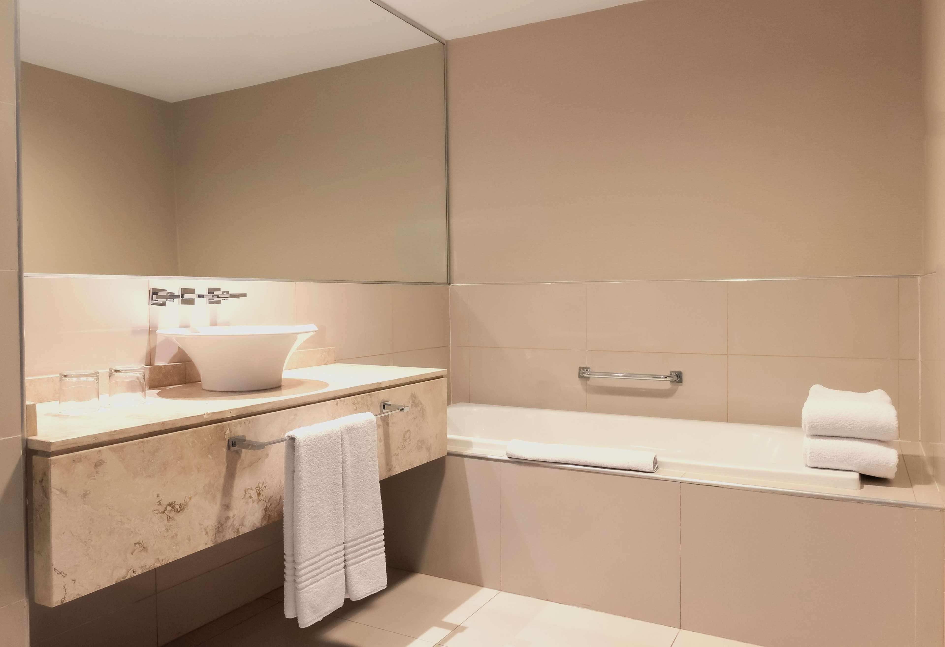 A modern bathroom with a marble vanity, a large mirror, a bathtub, and a towel rack.
