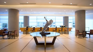 A spacious lobby with a central round table, multiple seating areas, and large windows offering a view of the cityscape. - Hilton Mendoza (Guaymallen)