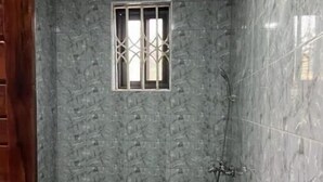 A bathroom with a marble wall, a window with bars, a shower, and a sink. - Serene Hostel Accra Bunk Bed Mixed dormitory (Adenta Municipality)
