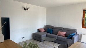A modern living room with a grey sectional sofa, a small round coffee table, and a potted plant. - Spacious T3 with balcony - close to town center (Touques)
