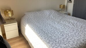 A bedroom with a bed, a nightstand, a lamp, and a wall-mounted light fixture. - Spacious T3 with balcony - close to town center (Touques)
