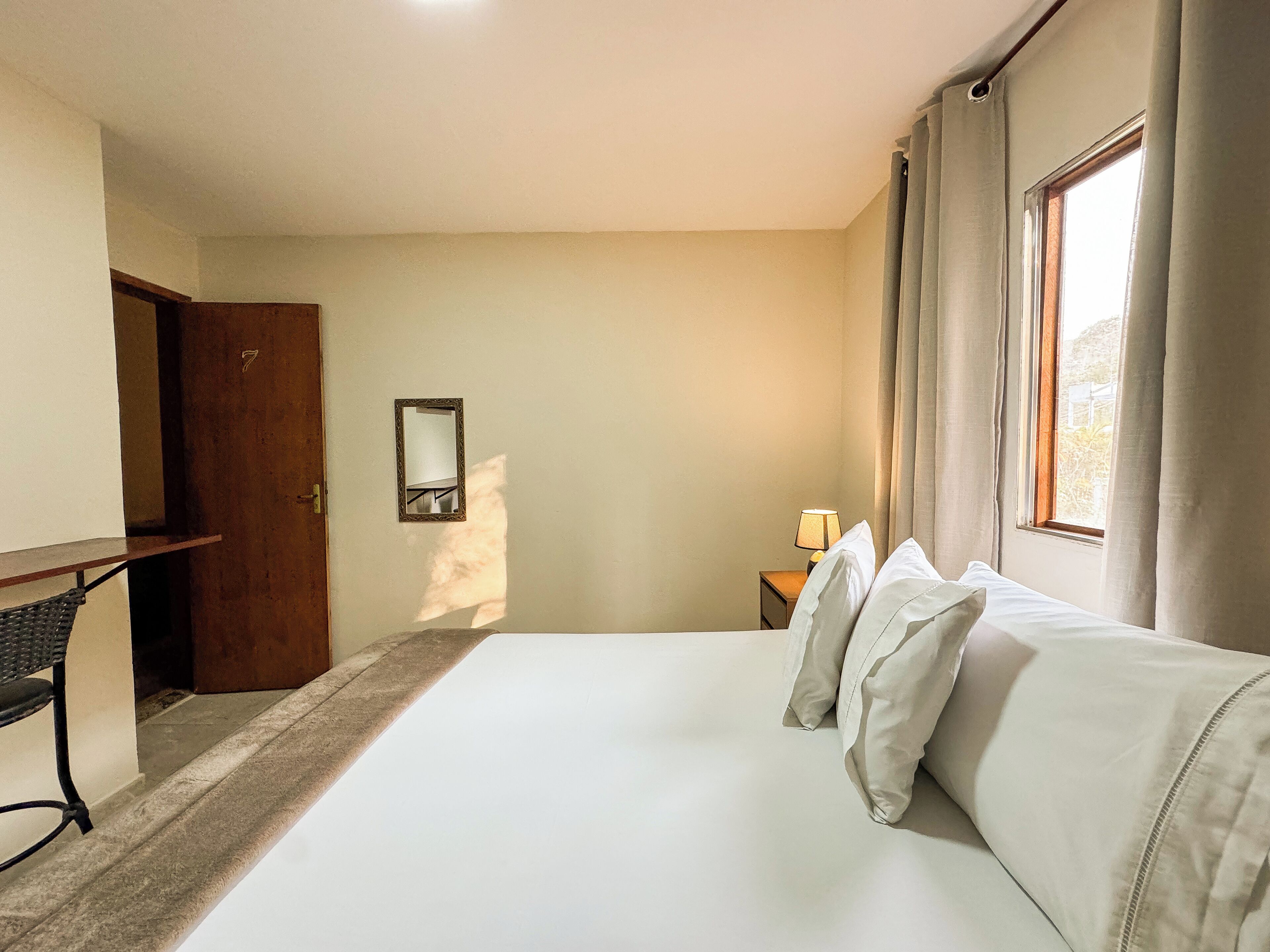 A hotel room with a bed, a desk, a nightstand, a mirror, and a window with curtains.