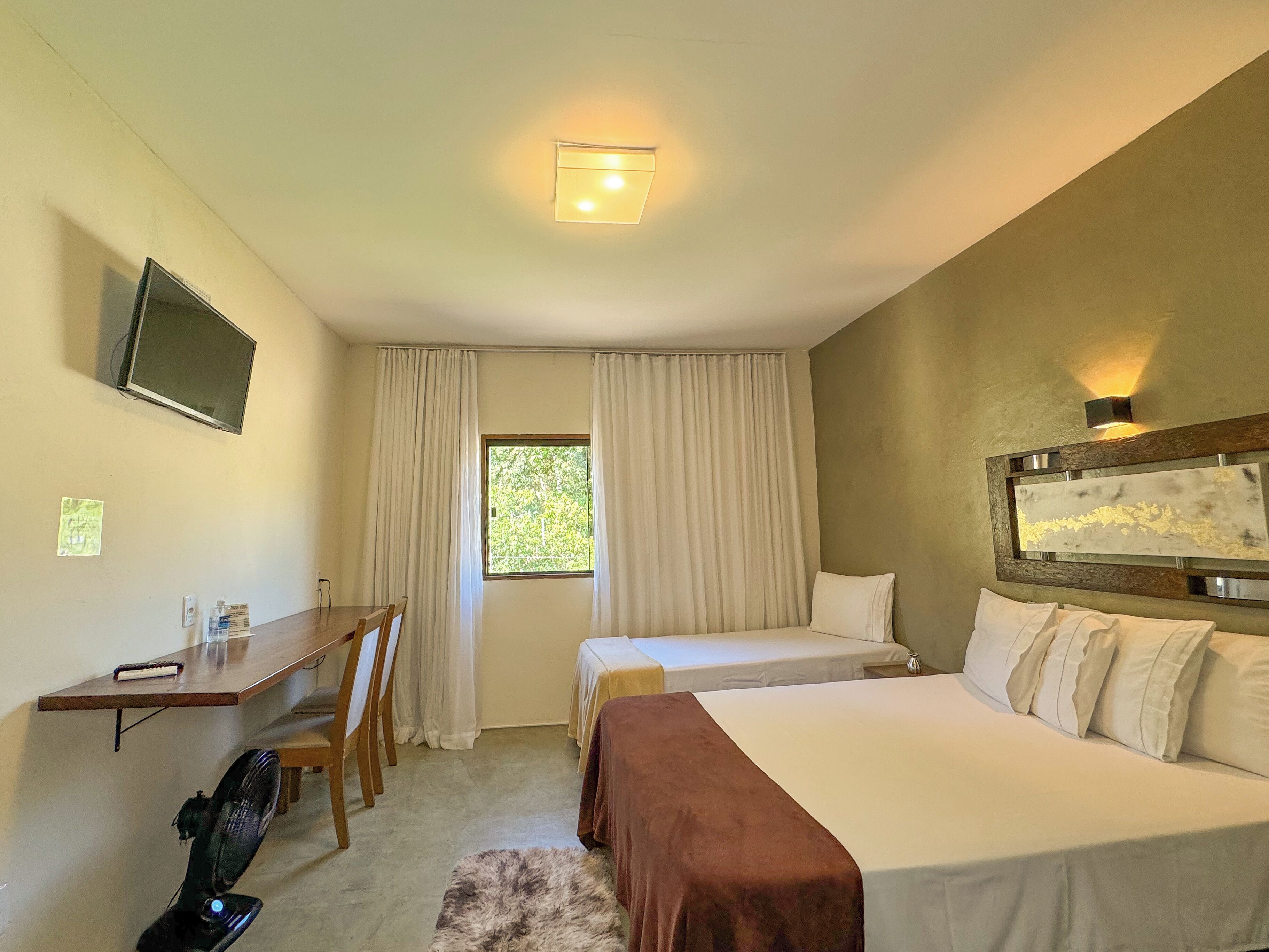 Habitación de hotel con cama, escritorio con silla, televisor montado en la pared y ventana con cortinas.