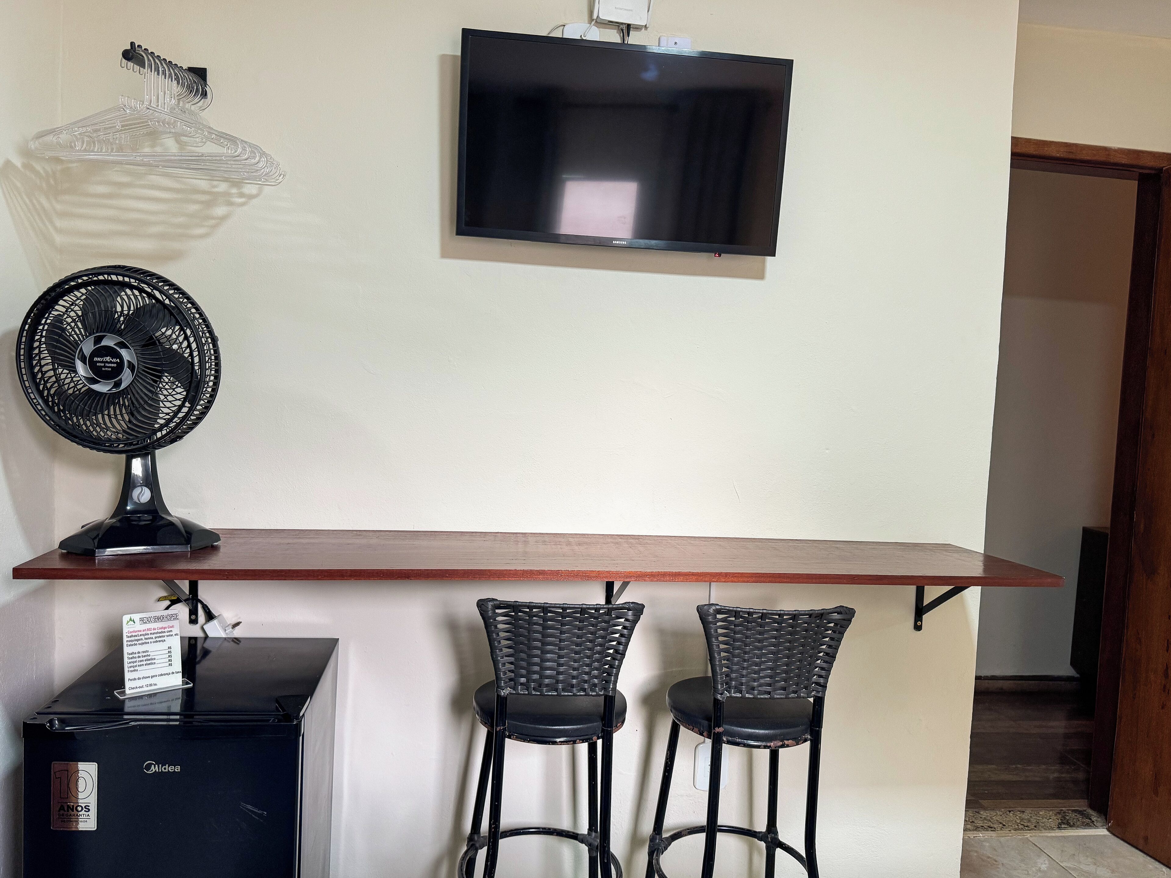 Un pequeño bar con televisor, ventilador y dos taburetes.