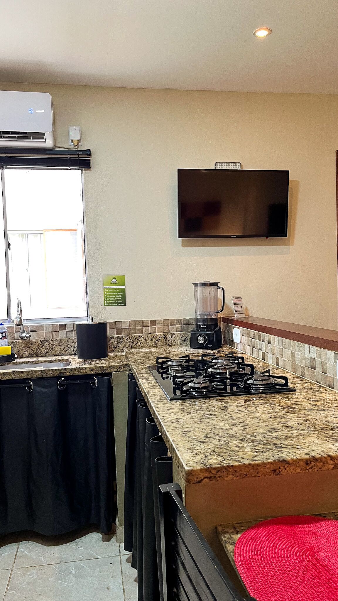 A kitchen with a gas stove, a blender, a flat-screen TV, and a window with a view.