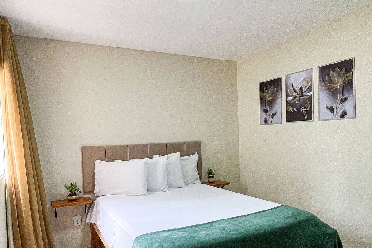 A neatly made bed with a green bedspread, a headboard, and a nightstand with a small plant.