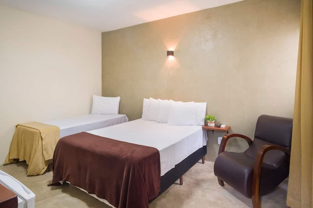 A hotel room with two single beds, a desk, a chair, and a nightstand with a lamp.