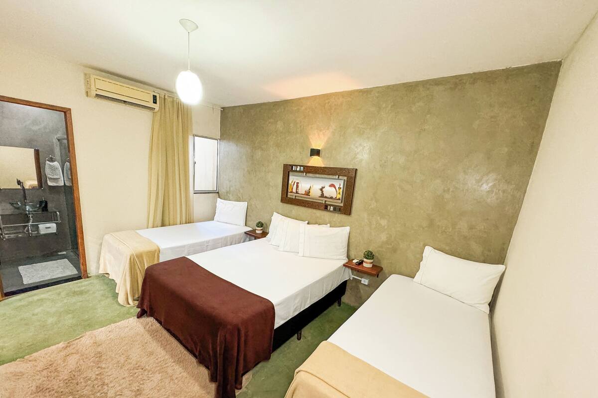 A hotel room with two beds, a small bedside table with a lamp, a wall-mounted picture, and a bathroom visible through an open door.