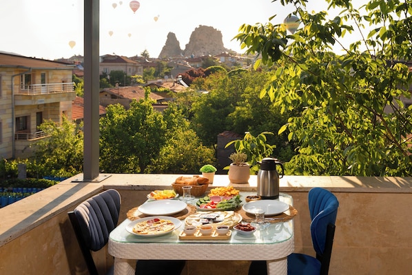 A balcony table set with food and a thermos, overlooking a cityscape with buildings and greenery. - Cappadocia Tuğhan Stone House (Nevsehir)