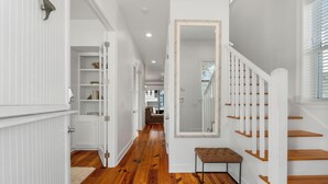 A hallway with wooden flooring, white walls, and a staircase with wooden steps and white railings.