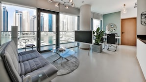A modern living room with a large window, a grey sofa, a TV, and a dining area. - Vida Residences Dubai Marina (Dubai)
