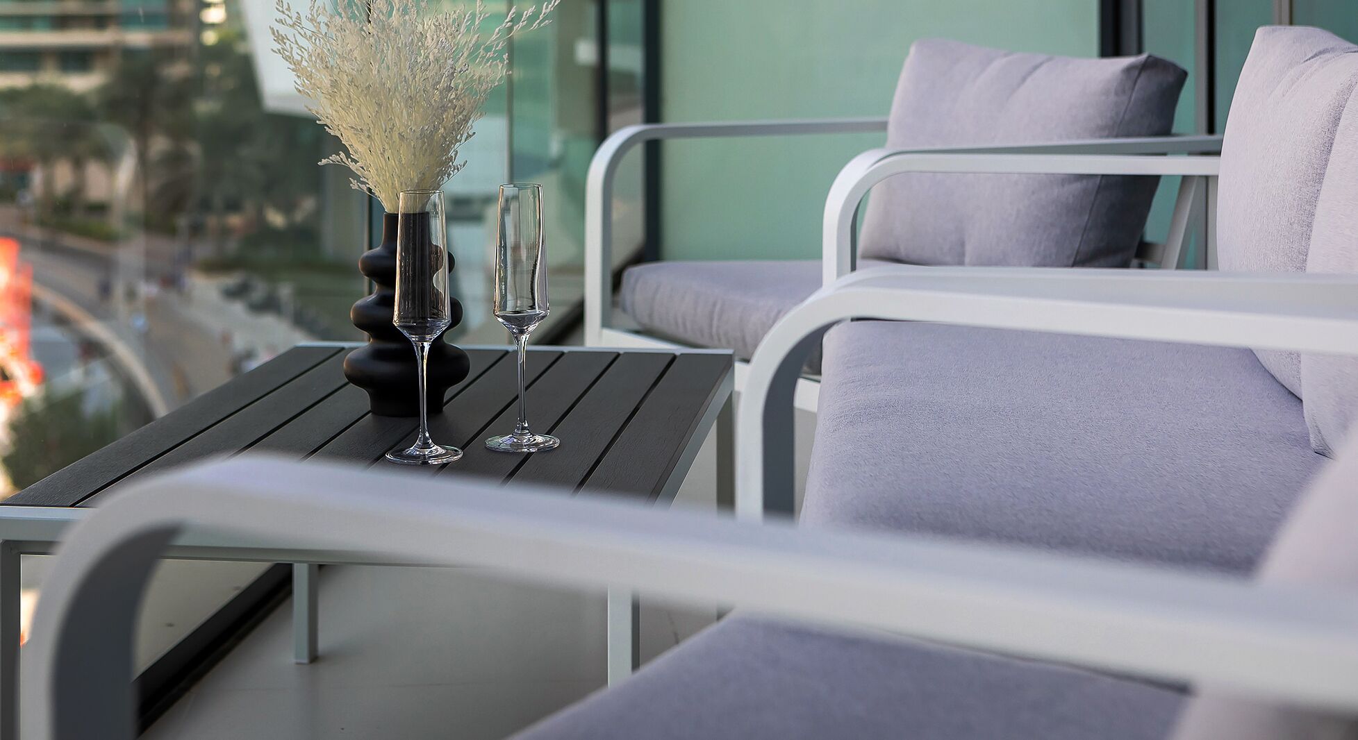 A balcony with a table, two chairs, and a vase with dried flowers.